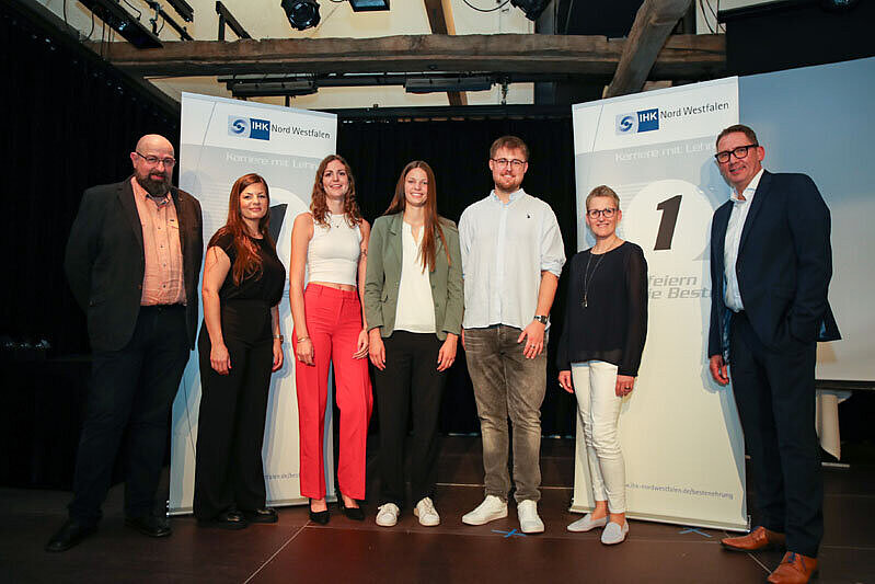 IHK Bestenehrung 7 Personen vor zwei großen IHK Plakaten.