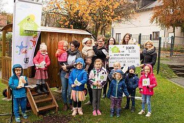 Sieger der Aktion grüner Kindergarten 2023 Kinder in einem Garten vor einem Spielhaus die Ein Plakat von Berief hochhalten.
