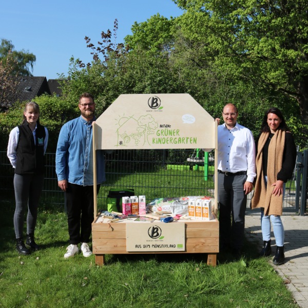 Hochbeet für die Kindertagespflege Eiderdaus Kindergarten-Mitarbeiter stehen lächelnd auf einer Wiese um ein Hochbeet mit Berief-Produktserie