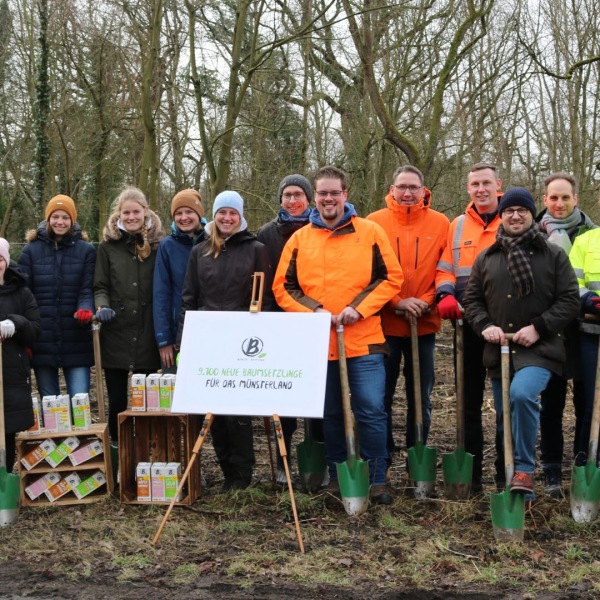 Bäume für Beckumer Wald Menschen stehen in warmer Kleidung mit Spaten auf einer Wiese.