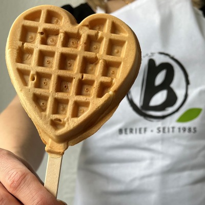 Vegane Waffelherzen ohne Zucker Jemand hält eine Waffel in Herzform an einem Stiel hoch