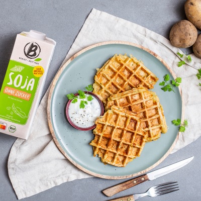 Herzhafte Kartoffel-Käse-Waffeln Runde Waffeln zusammen mit einem hellen Dip auf einem hellblauen Teller ganiert mit Kräutern