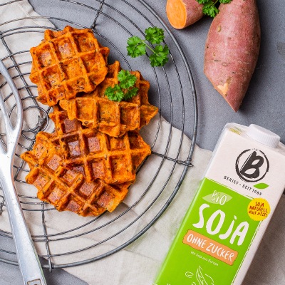 Herzhafte Süsskartoffelwaffeln Süsskartoffelwaffeln auf einem runden Gitter ganiert mit Kräutern