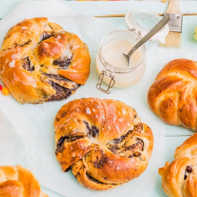Vegane Hefekränze mit Mohn Drei Mohn-Hefekränze zusammen mit einem Gläschen heller Glasur auf einem hellen Tischtuch