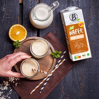 Frühstückssmoothie Vegan Zwei hellbraune Smoothies stehen auf einem runden Holzbrett mit Strohhalm und Dekoration