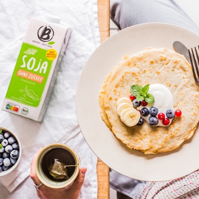 Einfache vegane Pfannkuchen Helle Pfannkuchen liegen auf einem weißem Teller garniert mit Obst und Basilikum