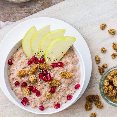 Porridge mit Apfel, Maulbeeren und Granatapfel Porridge mit Obst in einer weißen Schüssel