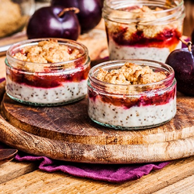 Pflaumen-Crumble mit Chia-Pudding Zwei Pudding-Desserts mit Topping in Glasschalen auf einem Holzteller mit Dekoration