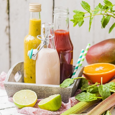 Veganer Rhabarber-Mandel-Smoothie Glasflaschen mit verschiedenfarbenen Smoothies auf einem Tablett mit Obstdekoration