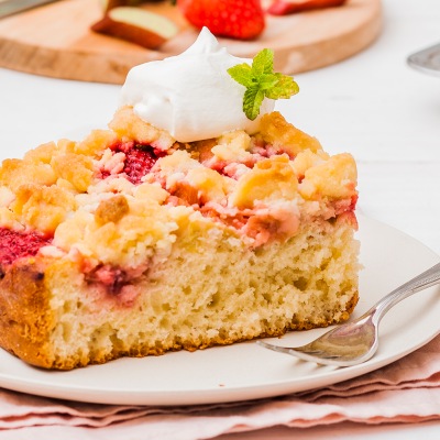 Rhabarber-Erdbeer-Streuselkuchen Streusselkuchen mit einem Klecks Sahne auf einem weißen Teller