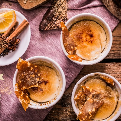 Crema Catalana Dessertcreme in kleinen, weißen Schalen mit Zimtstangen auf einem rosa Tischtuch