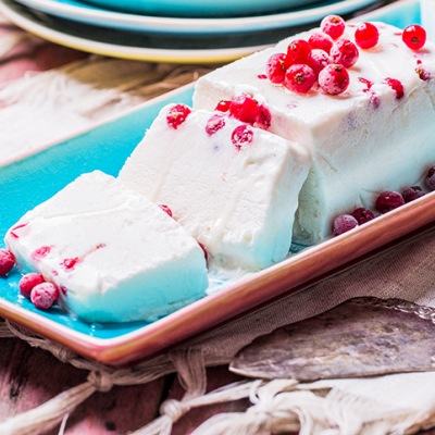 Agaven-Parfait mit Beeren Weißes Dessert auf einer länglichen Schale mit Früchtetopping auf einem Tisch