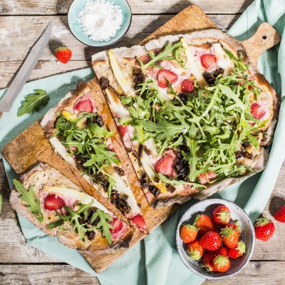 Flammkuchen mit Spargel und Erdbeeren Flammkuchen belegt mit Erdbeeren, Spargel und Rucola auf einem Holzbrett