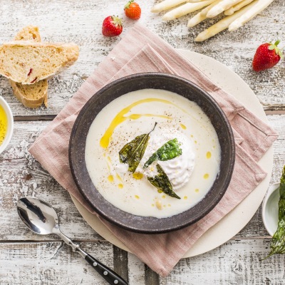 Spargelcremesuppe mit Bärlauch-Chips Cremfarbige Suppe mit Chips auf einem Tischtuch und Dekoration.