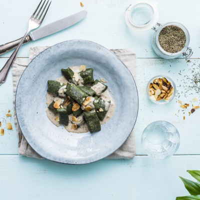 Spinat-Gnocchis mit Mandel-Thymian-Soße Spinat auf cremfarbiger Soße auf blauem Teller mit Dekoration.