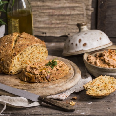 Moehrenbrot mit Tomaten-Streich Aufgeschnittenes, helles Brot mit Aufstrich auf einem runden Holzteller.