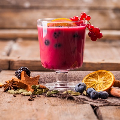 Wwinterlicher Beeren-Punch Rotes Getränk mit roten Beeren in einem Glas auf einem Holzbrett.