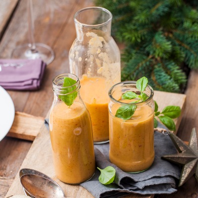 Exotisches Paprika Soja-Gazpacho Drei helle Suppen in Glasflaschen auf einem Holzbrett mit Dekoration.