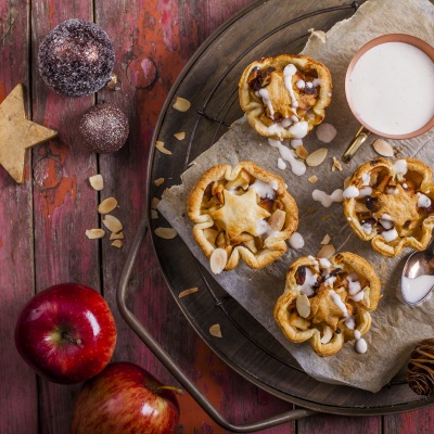 Bratapfel-Küchlein mit Vanillesauce Kleine Kuchen mit Apfel, Mandeln und Zuckerguß auf einem Teller mit Dekoration.