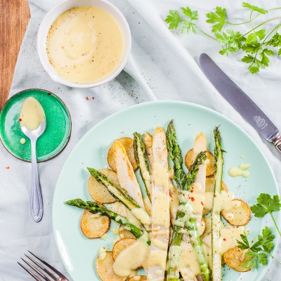 Sauceveganaise Spargel auf Kartoffelscheiben mit heller Sauce auf einem Teller mit Petersiele