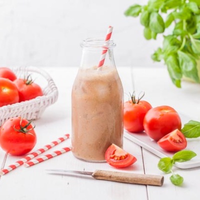 Tomaten-Soja-Smoothie Hellrotes Getränk in einer Glasflasche mit Strohhalm mit Tomaten und Basilikum-Dekoration.