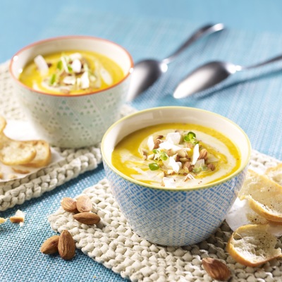 Möhren-Fenchelsuppe mit Kokosraspeln und Mandeln Gelbe Suppe in zwei Schalen mit Mandeltopping und Dekoration